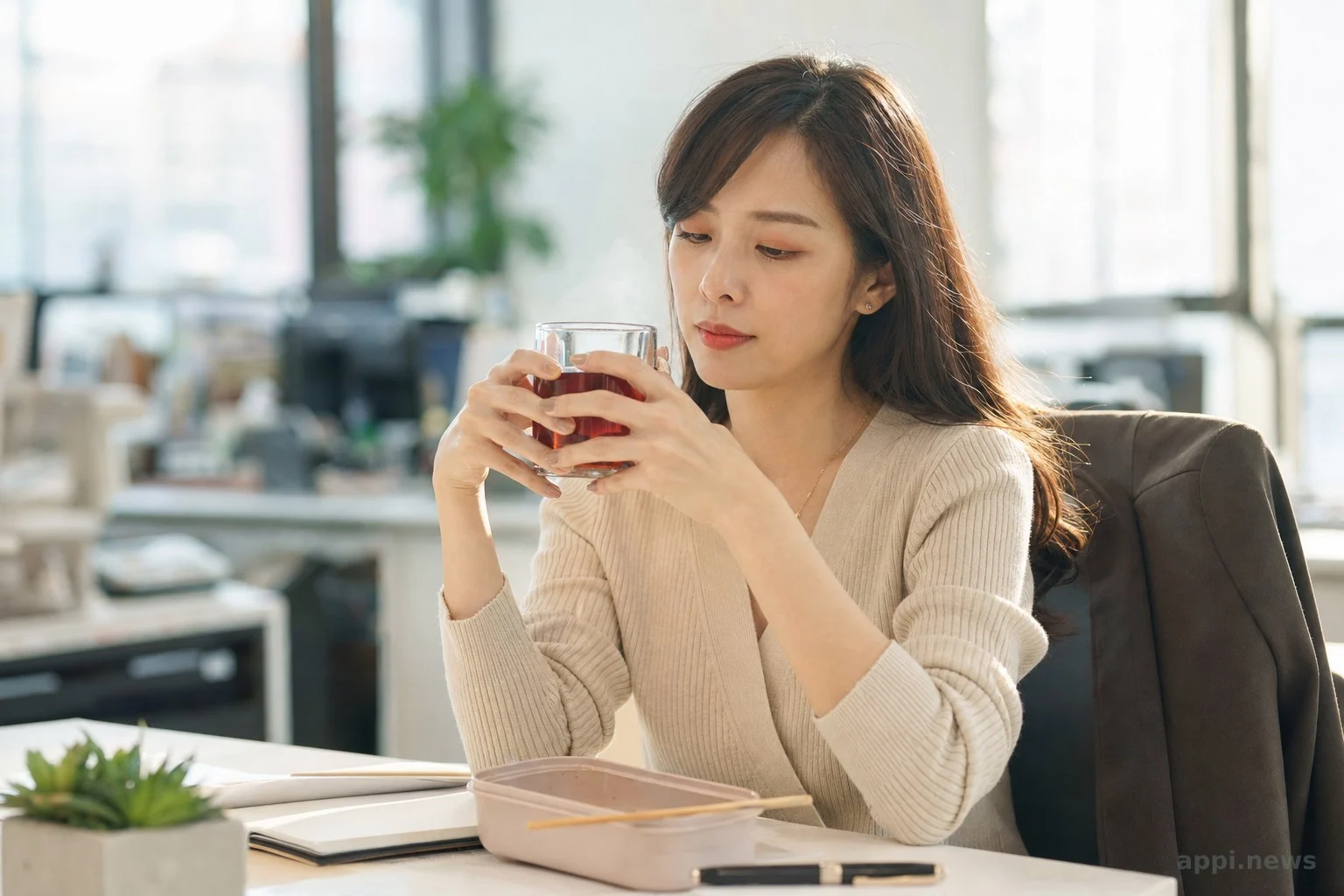 上班族在辦公桌前吃完便當後，端著一杯洛神花茶稍作休息的情境